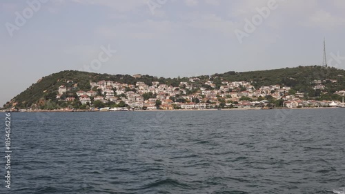 A scenic view of a coastal town on a hillside island, surrounded by water under a clear sky.