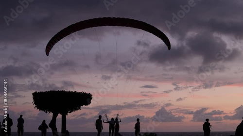 Silhouette of a paraglider preparing to launch against a vibrant sunset sky over the ocean in Turkey.