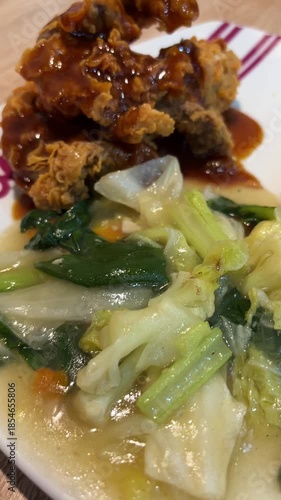 Indonesian meal with white rice, fried chicken in savory sauce, and sautéed vegetables served on plate