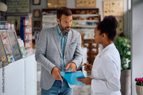 Mid adult man communicating with black female pharmacist in pharmacy.