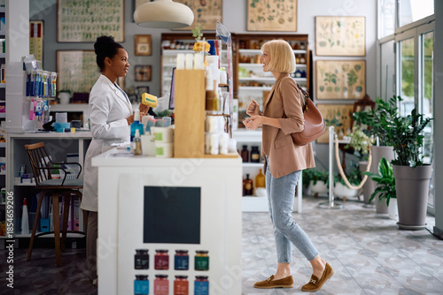 Happy black pharmacist advising her customer in choosing medicine in pharmacy.