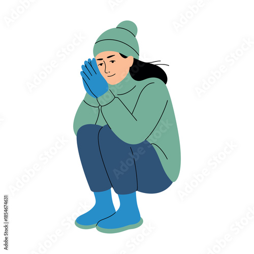 A person wearing a hat and gloves is crouching down to warm their hands.
