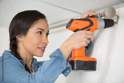 woman using rechargeable screwdriver to fix a curtain rail
