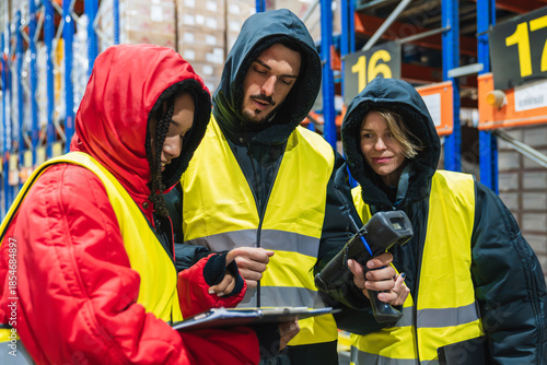 Group of diverse logistics employees wearing warm clothing and safety vests, scanning products and recording data in a freezer warehouse