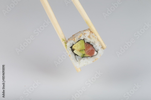 Maki saumon avocat tenu par des baguettes japonaises sur fond blanc