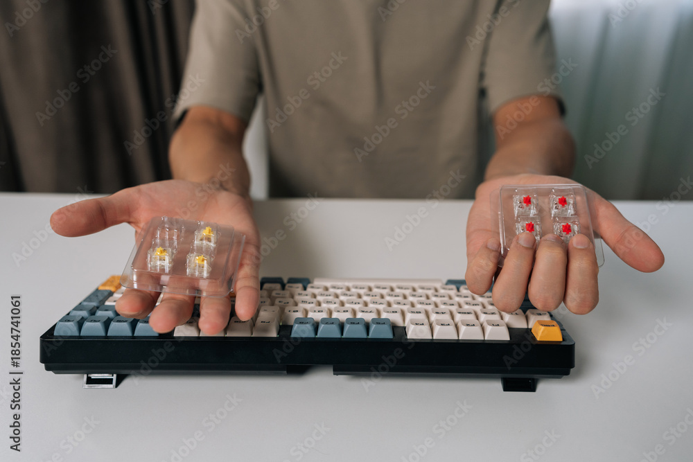 Fototapeta premium Man holding mechanical keyboard switches, choosing between different types for custom keyboard building and maintenance, repairing personal computer hardware, cropped shot portrait.