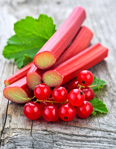 Fresh Rhubarb Stalks with Red Currants and Green Leaves on Wooden Table
