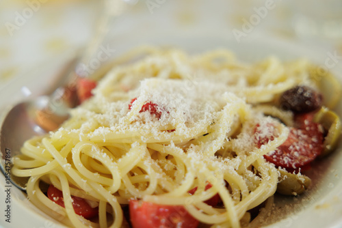 spaghetti con pomodorini a fette, olive e formaggio, visti parzialmente di profilo, tradizionale piatto leggero estivo italiano
