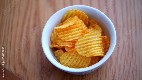 Crispy Rippled Potato Chips in White Bowl on Wooden Surface, Close-Up Shot, Top View