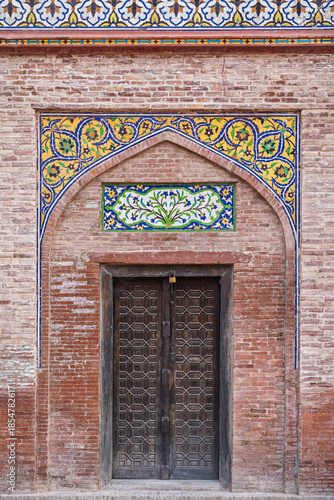View of arch door with kashi-kari or faience tile mosaic floral and geometric decor on ancient mughal Wazir Khan mosque, Lahore, Punjab, Pakistan