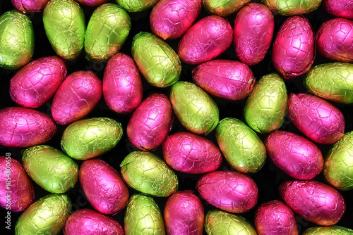 Pile or group of multi colored and different sizes of colourful foil wrapped chocolate easter eggs in lime green; yellow, and pink.