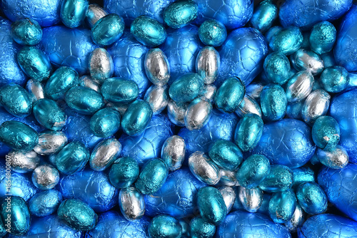 Blue,  silver and turquoise foil wrapped chocolate easter eggs, against a black background.