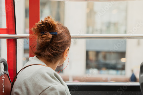 Photography A woman with her brown hair tied in a bun looks out the window of a red bus whil