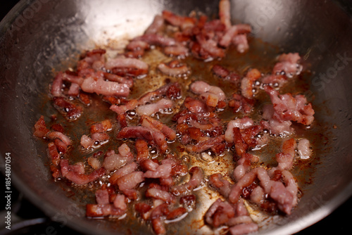 sizzling bacon strips frying in oil in a close-up view of a hot metal pan, capturing details of the crispy texture and rich, golden-brown color in a home kitchen setting, charred, tasty, seasoned