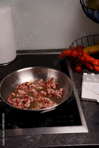 sizzling bacon strips cooking in stainless steel pan on induction stove, surrounded by fresh produce including tomatoes and bananas in modern kitchen setting, shimmering, equipment, counter, heat