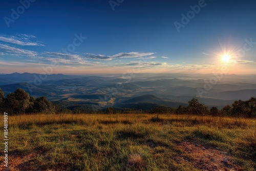 Golden Grassy Hillside Overlooks Misty Valley Cityscape At Sunrise Under Clear Blue Sky With Streaky Clouds