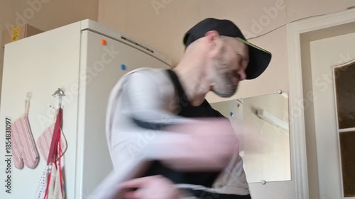 Energetic man in a black cap dancing joyfully in a domestic kitchen, vibrant with colorful refrigerator magnets. Captures a moment of carefree movement and daily life happiness.
