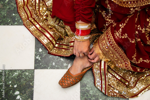 Indian woman in a traditional red dress sitting on checkered floor fixing her footwear