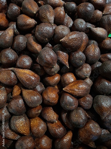A high-angle close-up shot of a pile of fresh salak or snake fruit with its unique brown scaly skin, displayed at a traditional tropical market.
