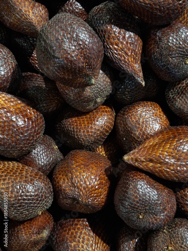 A high-angle close-up shot of a pile of fresh salak or snake fruit with its unique brown scaly skin, displayed at a traditional tropical market.