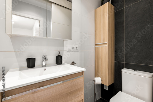 Wallpaper Mural Modern bathroom with a sleek design. Features a white sink, wooden cabinetry, a mirror, and a toilet. The walls are tiled in black and white. Torontodigital.ca