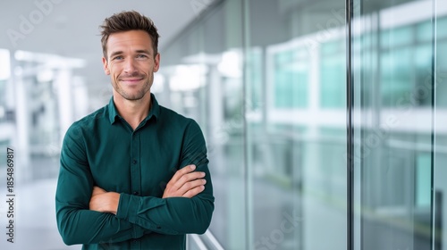 Confident young student, trade manager or businessman standing with arms crossed in office corridor, looking at camera. Male corporate employee or business professional posing indoors. Banner