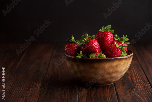 Fresh red strawberries in a rustic bowl on a dark wooden background. Front view