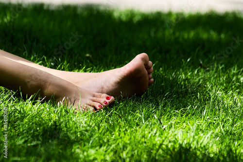 Outdoor Leisure: Bare Feet with Red Toenails Relaxing on Green Grass in Summer Nature Close-up