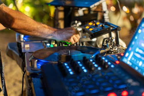 Primer plano de mano de DJ mezclando música en tocadiscos de vinilo y mesa de mezclas digital en club nocturno con luces azules.