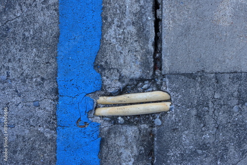 Section of two exposed yellow underground electrical PVC conduits, embedded within cracked gray concrete pavement. The conduits have become exposed due to damage to the surrounding concrete surface.