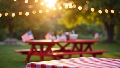 Red picnic table with American flags set for outdoor celebration. String lights glow in warm sunset light. Red checkered cloth covers foreground table. Summer gathering at dusk.