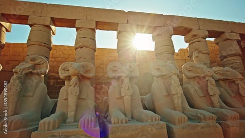 Row of ancient ram headed sphinx statues aligned in front of massive stone columns inside the Karnak Temple