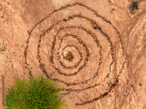 Aerial top down view of a spiral stone formation arranged on dry desert ground, natural land art pattern created with rocks forming a symbolic circular maze, representing mindfulness, balance, spiritu