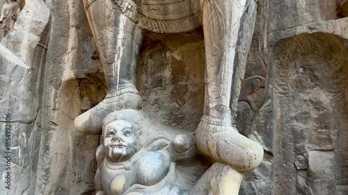 Statues of Vaisravana (Northern Heavenly King) and demon or evil spirit trampled underfoot on northern side of Fengxian Temple Cave at Longmen Grottoes, Luoyang, Henan, China. UNESCO World Heritage.
