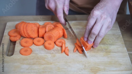 Hands slicing fresh carrots on wooden cutting board in home kitchen