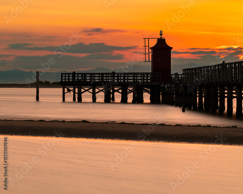 Vertical view of Faro Rosso lighthouse at dawn in Lignano Sabbiadoro, red beacon on pier with long exposure smoothing the Adriatic Sea, minimalist seascape with copy space, Italy travel concept.