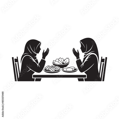 Two women in hijab praying over a meal at a wooden table