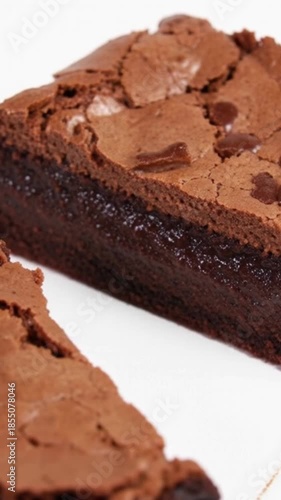 A chef's knife is gently pressed into a large, rectangular chocolate brownie, beginning to slice a perfect portion on a bright white surface.
