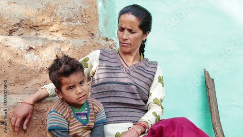 A young Indian village mother sits on the steps of her home with her little son, talking and playing together. The scene shows poverty, care, family bonding, and rural Uttarakhand life.