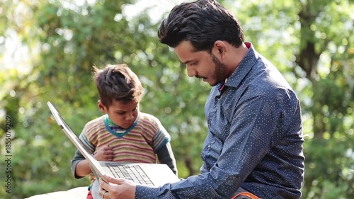 An Indian man teaches a poor village boy how to use a laptop outdoors in an Uttarakhand village. The scene highlights rural education, poverty, digital learning, and hope in mountain life.