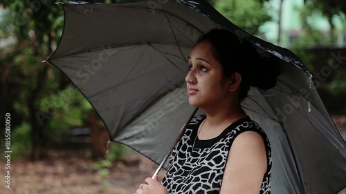 A young woman enjoys rainfall under an umbrella in an Uttarakhand village. The moment reflects rural lifestyle, poverty, monsoon season, nature connection, and simple mountain life in India.