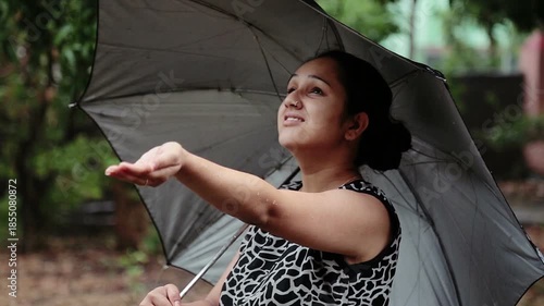 A young woman enjoys rainfall under an umbrella in an Uttarakhand village. The moment reflects rural lifestyle, poverty, monsoon season, nature connection, and simple mountain life in India.