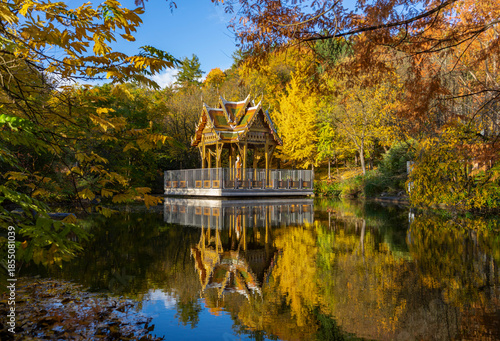 Herbst im Westpark, München: Thailändische Sala, Tempel mit Buddha Statue - farbenfrohe, bunte Bäume und Spiegelung im See