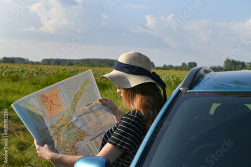 Rear view shot of couple driving on country road. Woman holding map and showing the route map to her boyfriend driving the car. Couple on a road trip.
