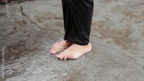 Close up of a woman’s bare feet standing on a wet floor during rain in an Uttarakhand village. The scene reflects poverty, rural life, simplicity, and monsoon lifestyle in India.