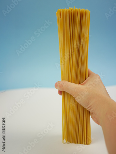 Wallpaper Mural Closeup of hand gripping a bundle of long dry spaghetti pasta in front of soft blue background, simple Italian food ingredient image for cooking themes. Pro Photo Torontodigital.ca