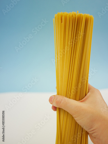 Wallpaper Mural Human hand holding a tall bundle of uncooked spaghetti pasta against blue and white background, food concept of dry Italian noodles and cooking ingredients Torontodigital.ca