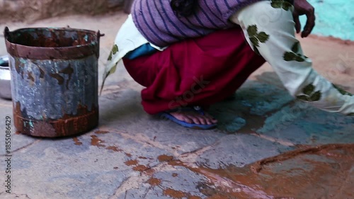 A rural woman applies cow dung to the floor in an Uttarakhand village, showing poverty, traditional practices, hygiene methods, and daily rural lifestyle in an Indian mountain community.