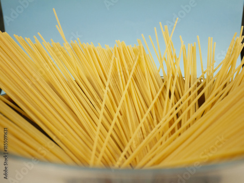 Wallpaper Mural Closeup top edge view of uncooked spaghetti fanned out inside metal pot on blue background, detailed texture of long dry pasta for Italian food concepts Torontodigital.ca