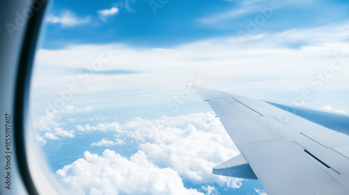 View from airplane window showing aircraft wing above clouds in bright blue sky. Travel, aviation and business trip concept with copy space